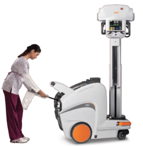 A woman wearing scrubs pushes a large, wheeled portable X-ray machine. Portable X-ray machines offer a number of benefits that increase patient care.